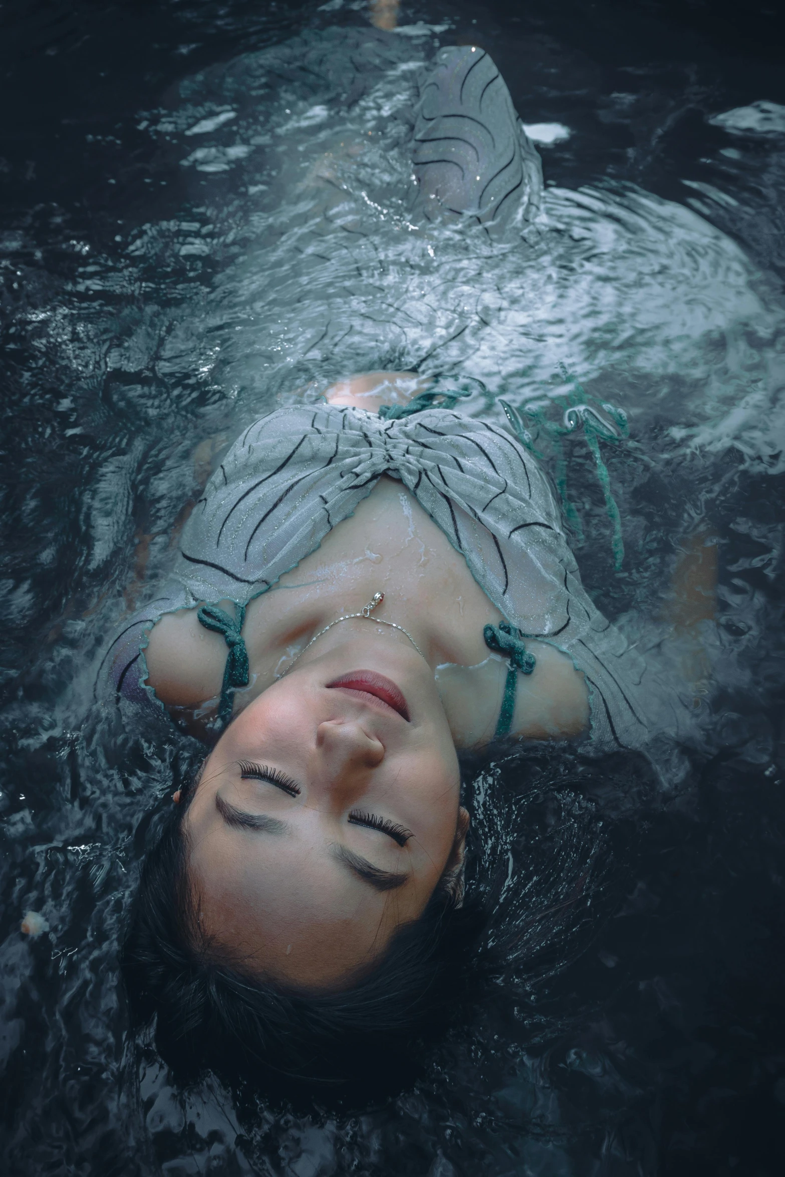 a woman laying on top of a body of water, looking down on the camera