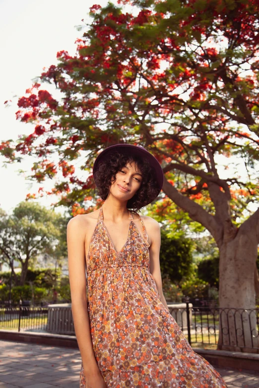 a woman in a dress and hat standing next to a tree, orange halter top, floral dream, prana, hollywood promotional image