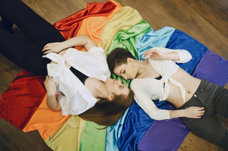 a couple of women laying on top of a colorful blanket, by Julia Pishtar, renaissance, lgbt flag, anna nikonova aka newmilky, indoor picture, ad image