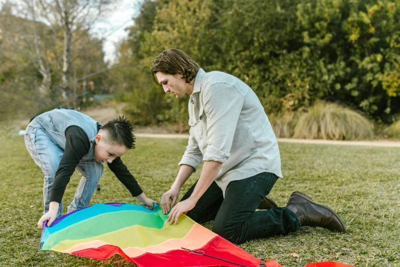 a woman and a child are playing with a kite, by Jacqui Morgan, unsplash, conceptual art, non-binary, sydney park, lying down, lgbt