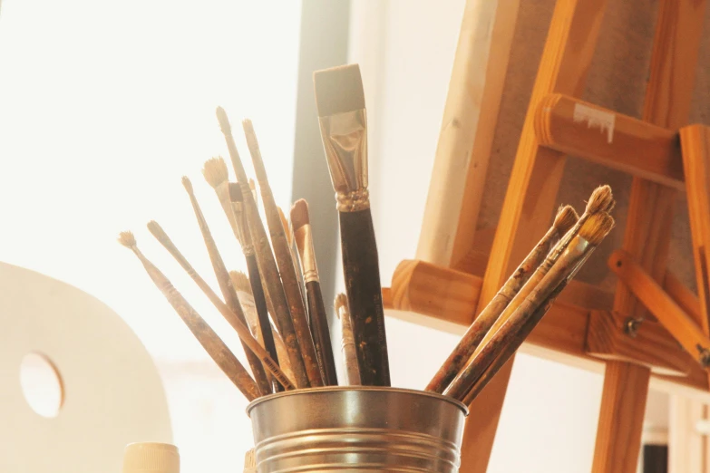 a cup that has some paint brushes in it, a photorealistic painting, unsplash, process art, golden hour sunlight, close - up studio photo, brown, easel