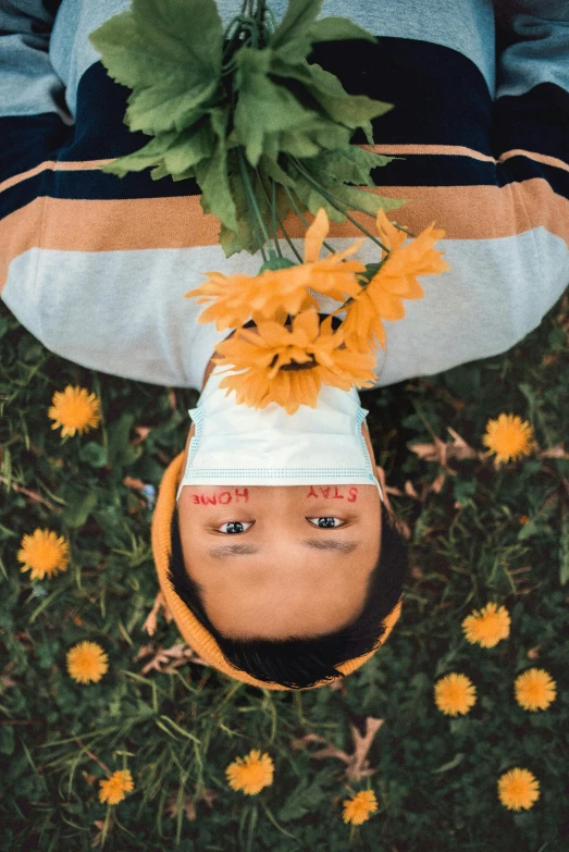 a person laying in the grass with a bunch of flowers on their head, an album cover, trending on pexels, hyperrealism, yellow pupils, upsidedown, playboi carti portrait, high angle shot