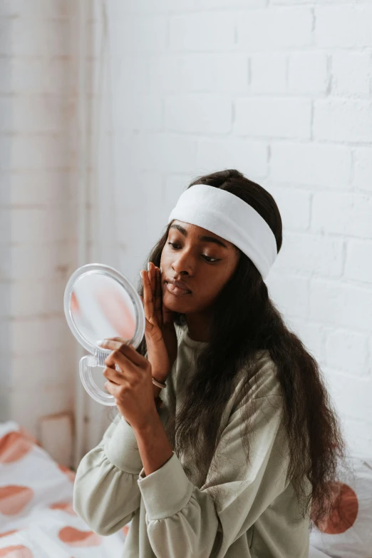 a woman sitting on a bed in front of a mirror, trending on pexels, wearing a headband, silicone skin, with brown skin, doctors mirror