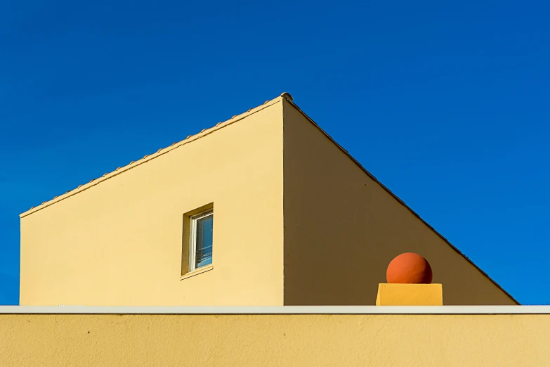a red object sitting on top of a yellow building, by Jan Rustem, postminimalism, blue and orange tones, ocher, blue - yellow sky, stucco walls