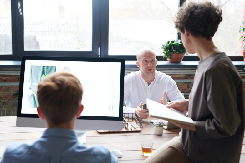 a group of people sitting around a wooden table, a picture, in front of a computer, profile image, man sitting facing away, professional image