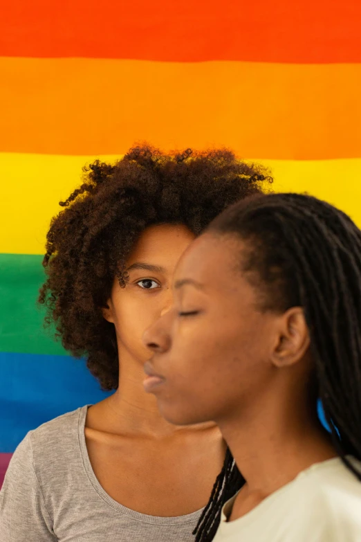 two women standing next to each other in front of a rainbow flag, by Lily Delissa Joseph, trending on pexels, renaissance, ( ( brown skin ) ), half face, two young men, on clear background