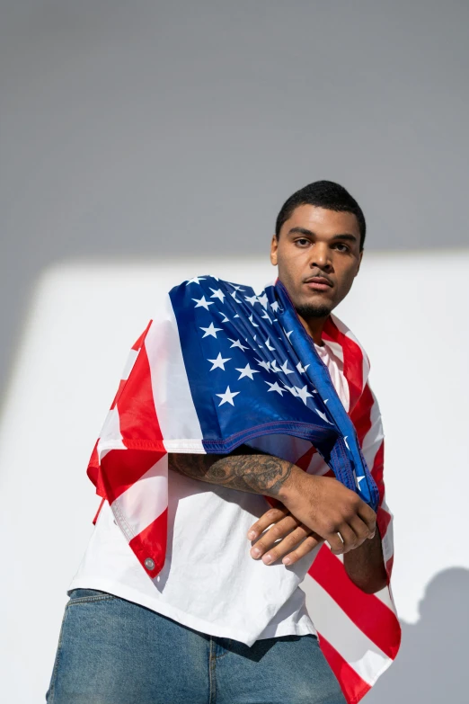 a man standing in front of a white wall holding an american flag, an album cover, inspired by Frank Mason, unsplash, yung lean, muhammad ali, handsome man, pictured from the shoulders up