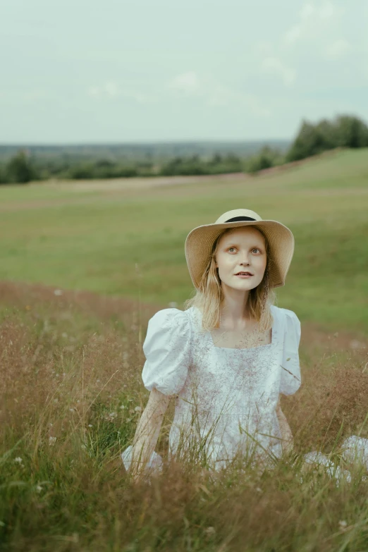 a woman sitting in a field with a hat on, an album cover, by Anna Boch, pexels, renaissance, evanna lynch, pale fair skin, press shot, hillside