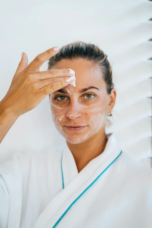 a woman putting a facial mask on her face, by Julian Allen, large forehead, her face is coated in a whitish, oceanside, giorgia meloni