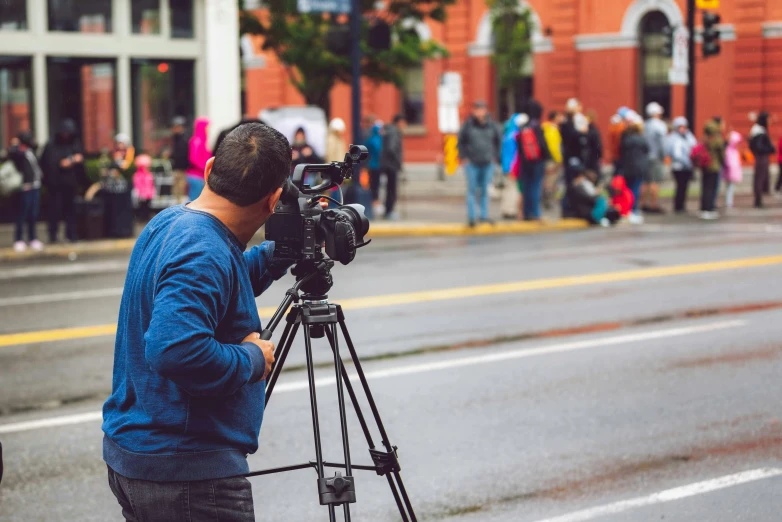 a man that is standing in the street with a camera, pexels, video art, news broadcast, people watching, tripod, performing