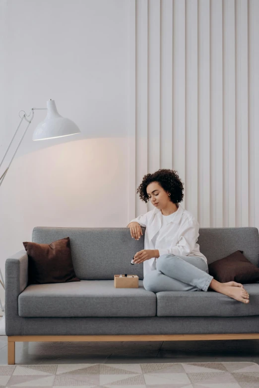 a woman sitting on a couch in a living room, pexels contest winner, minimalism, samsung smartthings, comfy lighting, promo image, having a snack