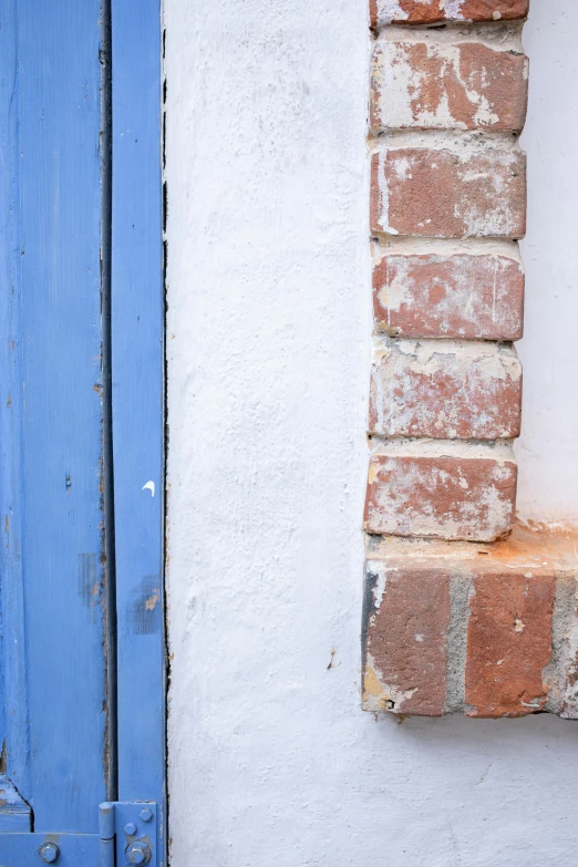 a cat sitting on a window sill in front of a blue door, inspired by Rachel Whiteread, unsplash, abstract detail, bricks, greek elements, close up image