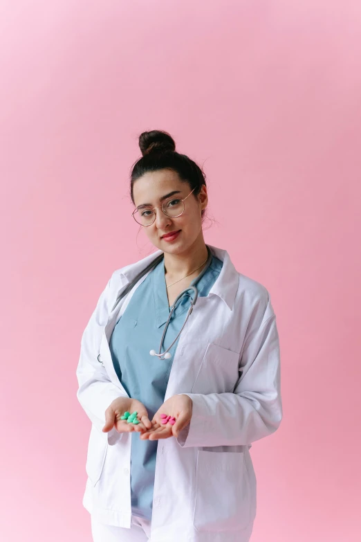 a woman in a lab coat standing in front of a pink background, pexels contest winner, antipodeans, made of candy, dilraba dilmurat, healthcare worker, the woman holds more toys