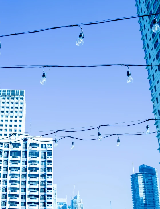 a city street filled with lots of tall buildings, inspired by Cerith Wyn Evans, unsplash, light and space, blue lamps on the ceiling, holiday, roof garden, string lights