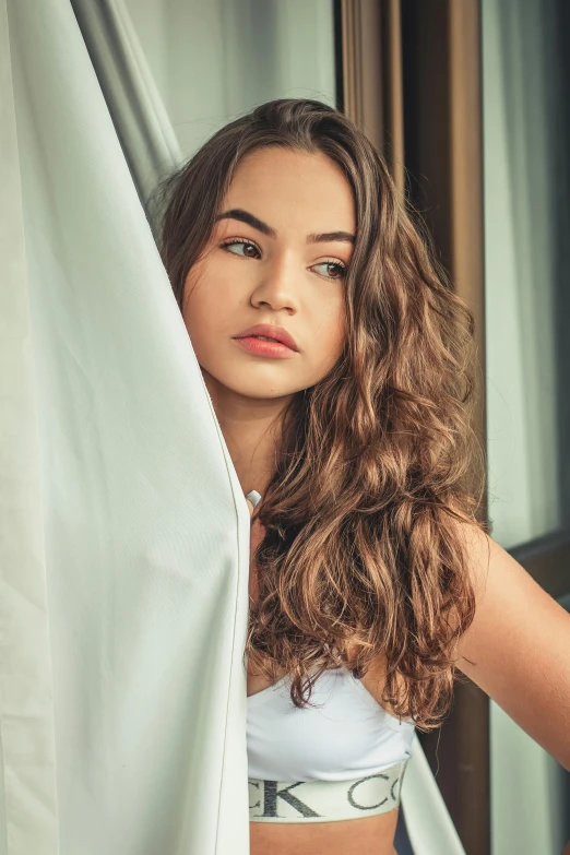 a beautiful young woman standing in front of a window, a picture, trending on unsplash, renaissance, medium - long curly brown hair, isabela moner, fully covered in drapes, anna nikonova aka newmilky