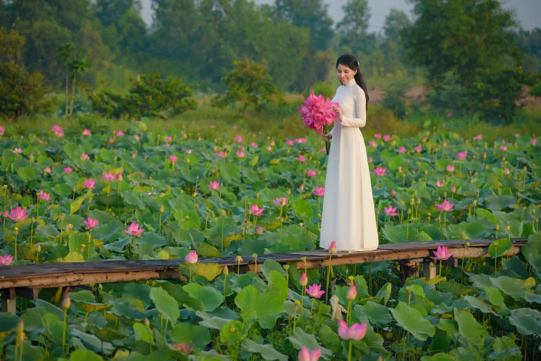 a woman in a white dress standing in a field of flowers, inspired by Cui Bai, visual art, pink lotus queen, near a jetty, ao dai, festivals