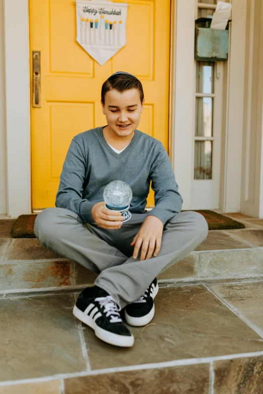 a man sitting on the steps in front of a yellow door, inspired by John Luke, instagram, holding a boba milky oolong tea, blue gray, teen boy, holding a glowing orb