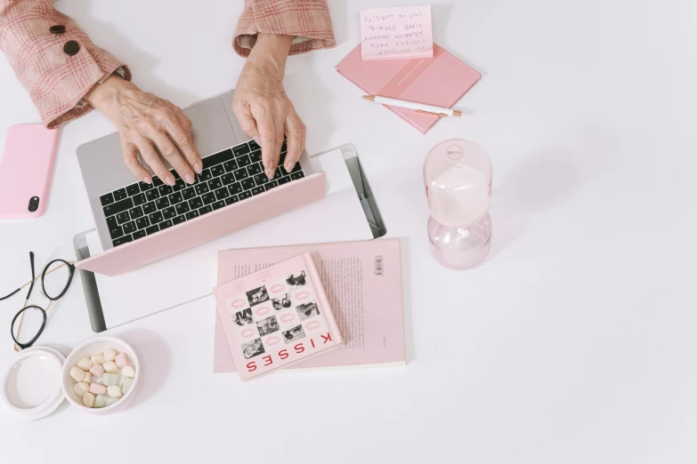 a woman sitting at a desk typing on a laptop, trending on pexels, minimal pink palette, flatlay book collection, background image, 2 k aesthetic