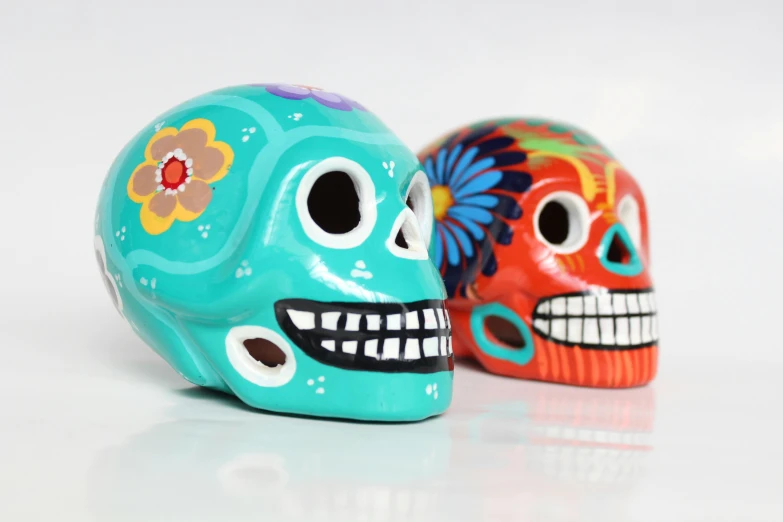 a couple of skulls sitting next to each other, by Juan O'Gorman, trending on pixabay, toyism, turquoise and venetian red, front profile shot, avatar image, orange and cyan paint decals