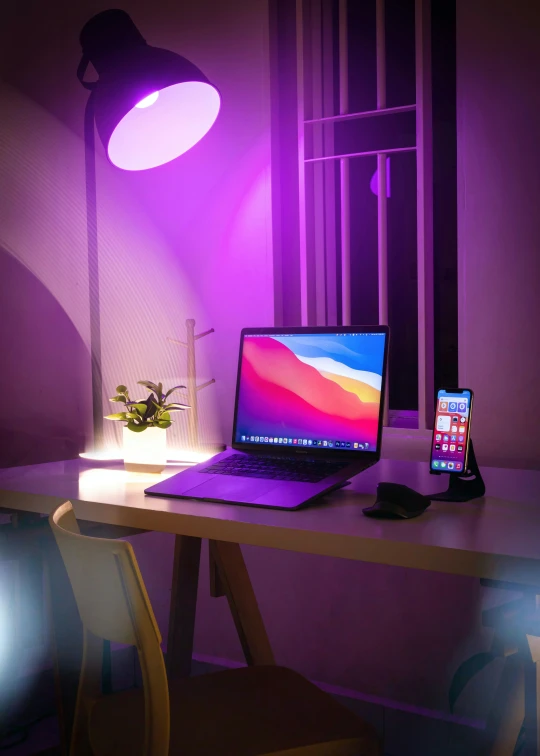 a laptop computer sitting on top of a wooden desk, by Adam Rex, light and space, brightly lit purple room, rgb wall light, apartment of an art student, high-tech devices