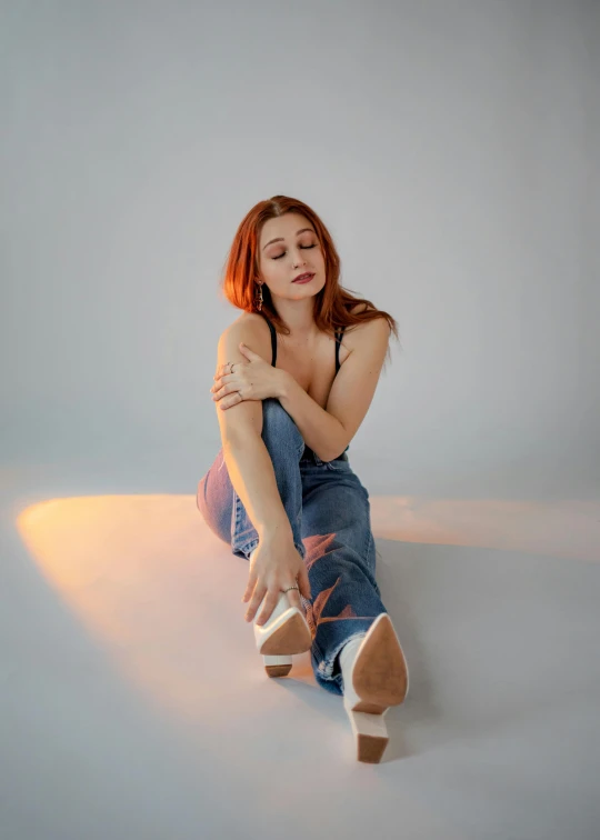 a woman sitting on top of a white floor, an album cover, inspired by Elsa Bleda, trending on pexels, redhead woman, jeans, translucent skin, glowing