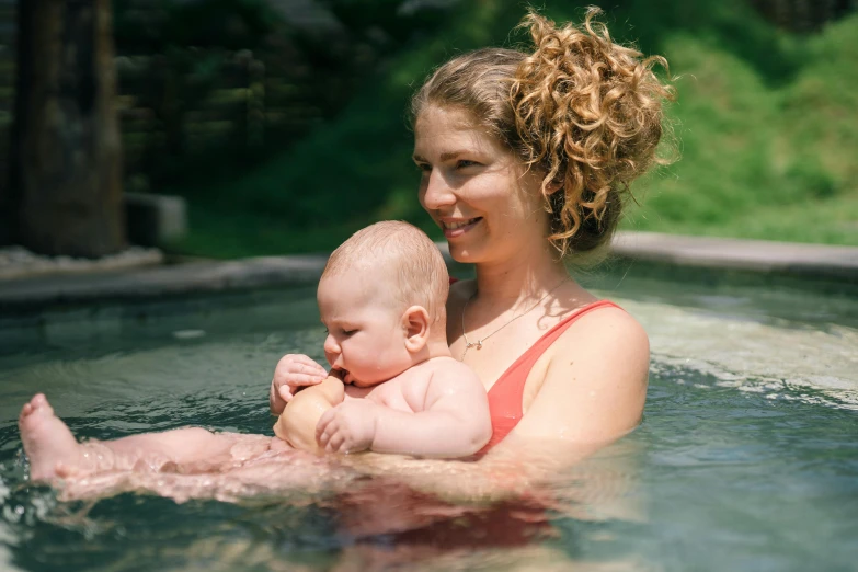 a woman holding a baby in a pool, a portrait, unsplash, may gibbs, thumbnail, seasonal, brown