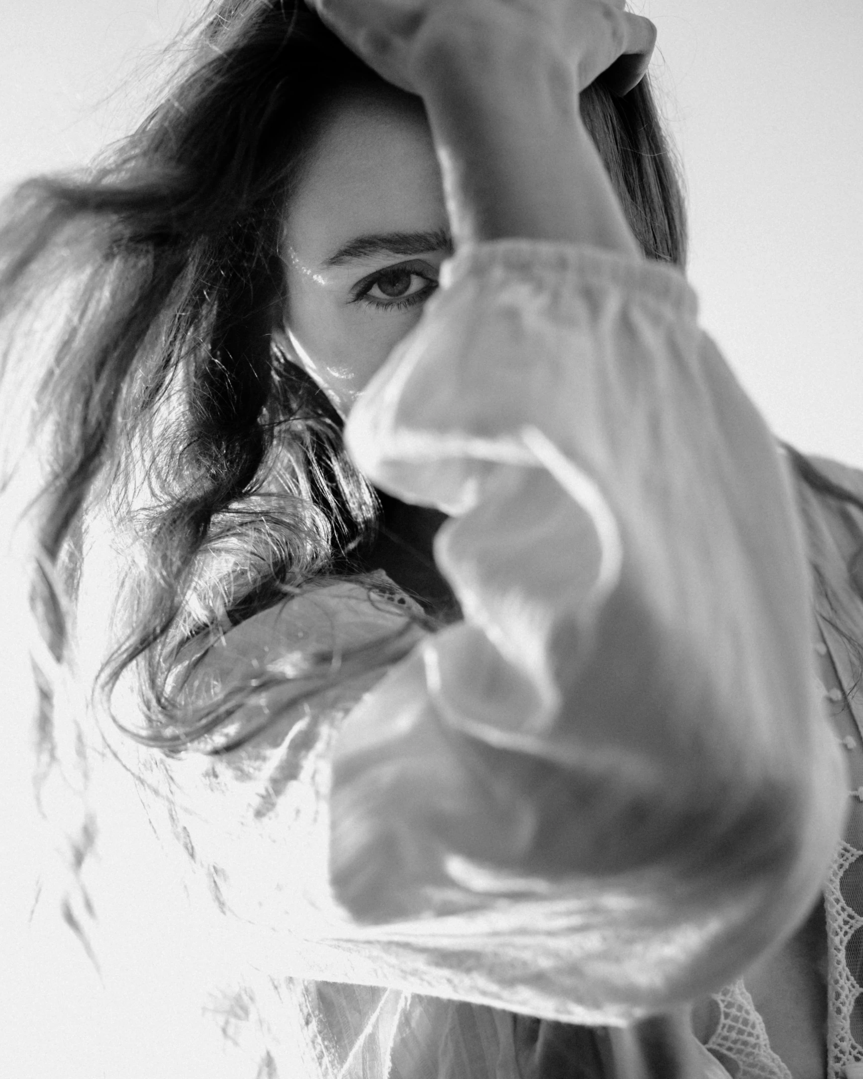 a black and white photo of a woman with long hair, a black and white photo, unsplash, white cloth in wind shining, lilly collins, pointing at the camera, close - up photograph