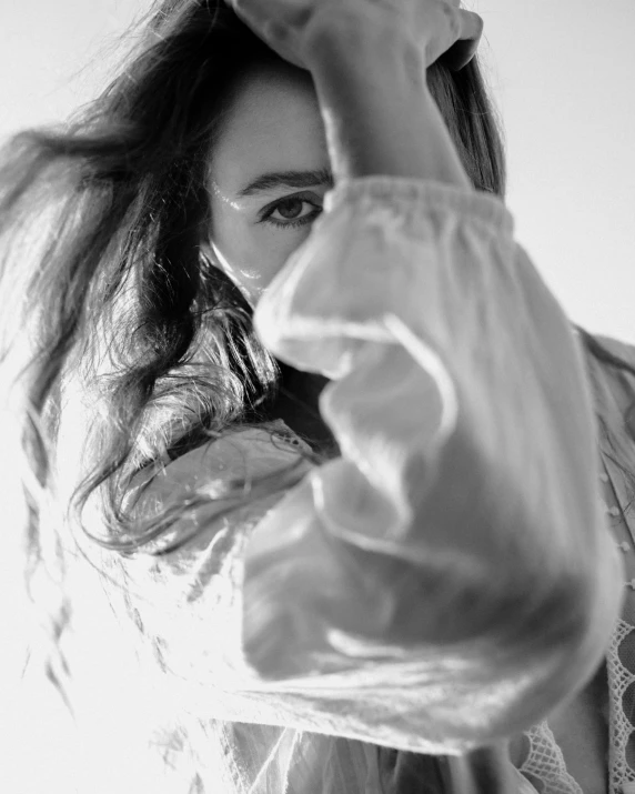 a black and white photo of a woman with long hair, a black and white photo, unsplash, white cloth in wind shining, lilly collins, pointing at the camera, close - up photograph