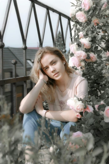 a woman sitting in front of a bush of flowers, a picture, by Adam Marczyński, pexels contest winner, portrait of white teenage girl, at the terrace, faded pink, a blond