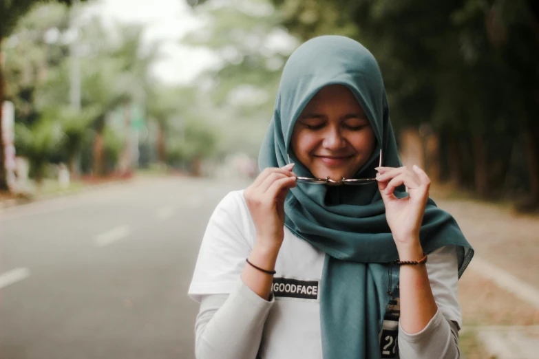 a woman standing on the side of a road, inspired by JoWOnder, pexels contest winner, hurufiyya, face covered, taking control while smiling, white and teal garment, malaysian