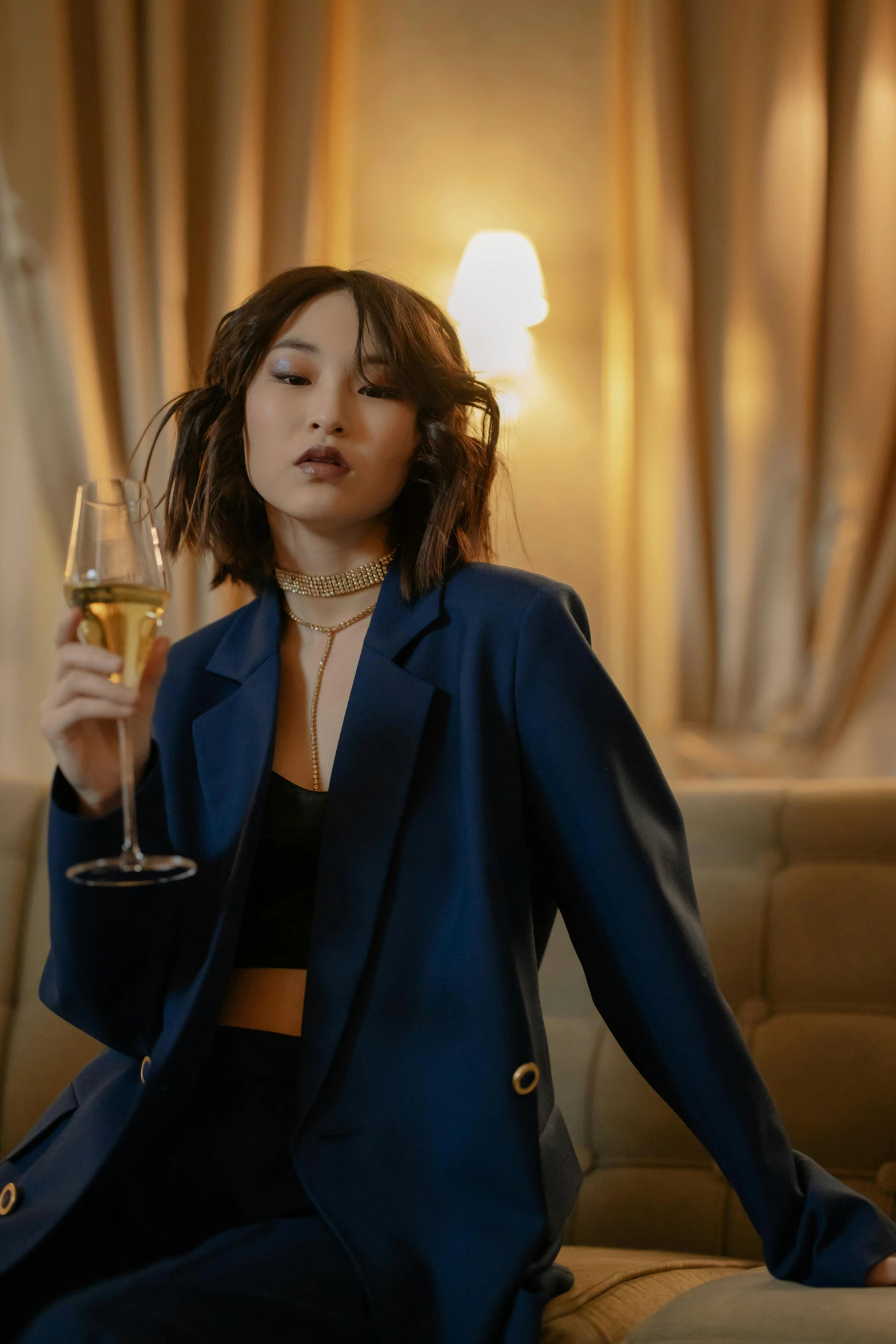 a woman sitting on a couch holding a glass of wine, an album cover, inspired by Zhou Wenjing, trending on pexels, wearing blue jacket, wearing fashion suit, nightlife, celebration