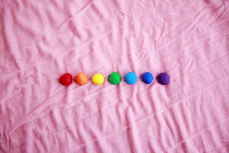 rainbow colored balls arranged in a row on a pink blanket, by Olivia Peguero, trending on pexels, modelling clay, chakras, buttons, shot on sony a 7