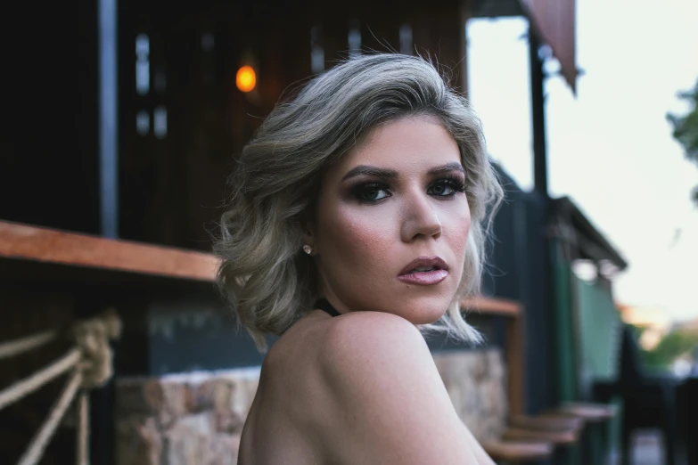 a woman posing for a picture in front of a building, inspired by Elsa Bleda, trending on pexels, realism, sexy face with full makeup, ash blond hair, dark backdrop, background bar