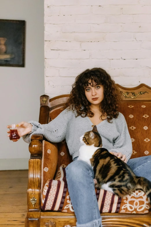 a woman sitting on a couch with two cats, an album cover, by Julia Pishtar, pexels contest winner, renaissance, curly bangs, holding a drink, casual pose, ayanamikodon and irakli nadar