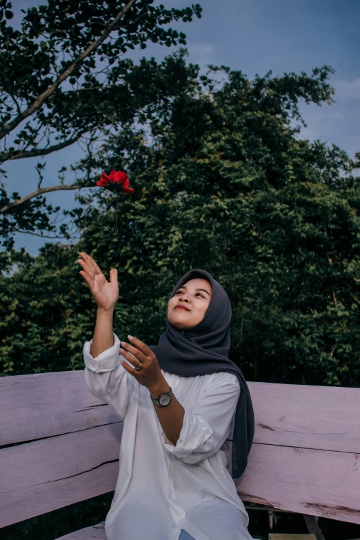 a woman sitting on top of a wooden bench, by Ismail Acar, pexels contest winner, hurufiyya, many birds and roses fly around, hijab, throwing cards in the air, kuntilanak on tree