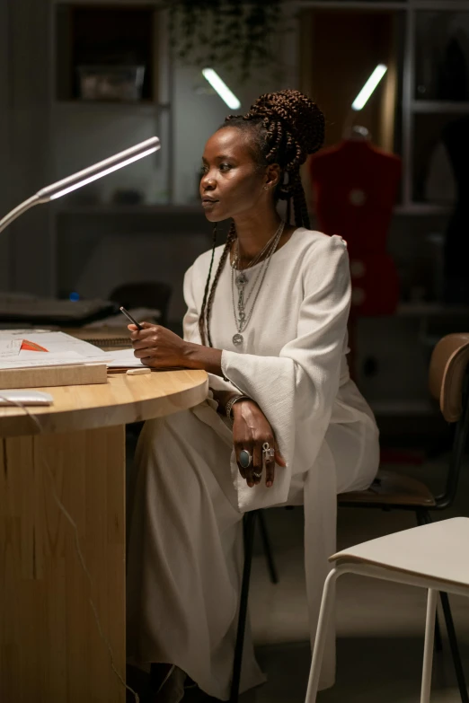 a woman sitting at a table with a lamp on, inspired by Afewerk Tekle, process art, intricate led jewellery, architect, adut akech, carefully crafted