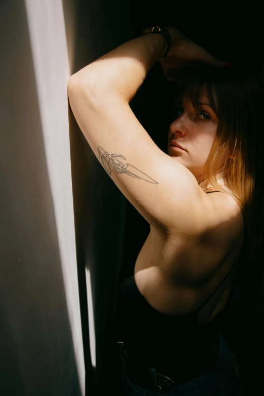 a woman with a tattoo on her arm leaning against a wall, a tattoo, inspired by Elsa Bleda, pexels contest winner, renaissance, she is wearing a black tank top, window light, armpit, androgynous person