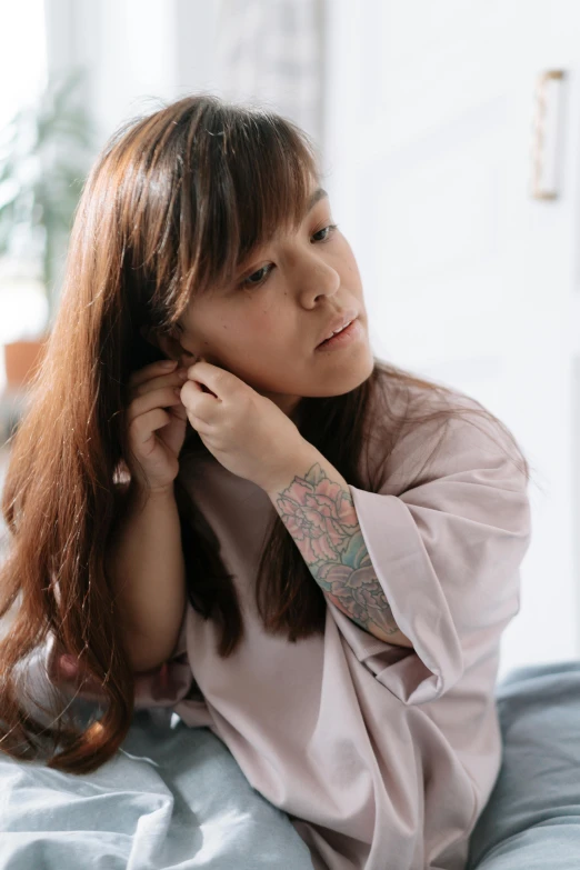 a woman sitting on a bed with a tattoo on her arm, inspired by Ruth Jên, trending on pexels, tinnitus, asian face, pondering, brown haired