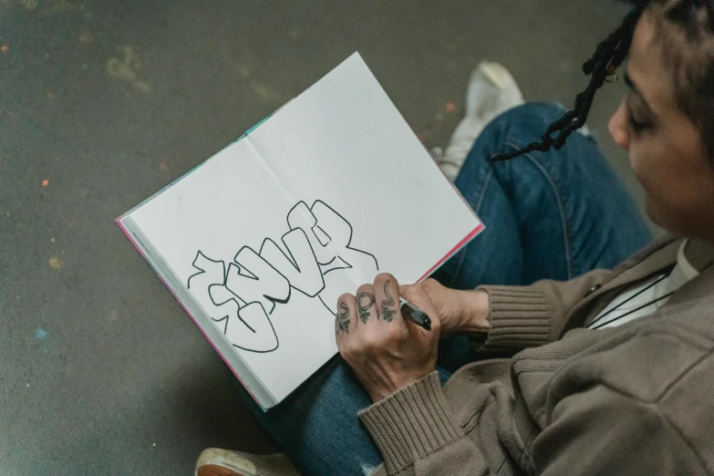 a woman sitting on the ground reading a book, a drawing, trending on pexels, graffiti, art in the style of joshy sly, concrete poetry, he is holding a large book, slay