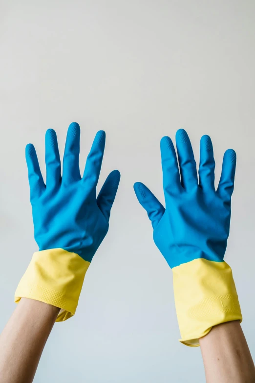 two hands wearing blue and yellow rubber gloves, a cartoon, pexels, plasticien, on grey background, bright blue, at home, hands behind back