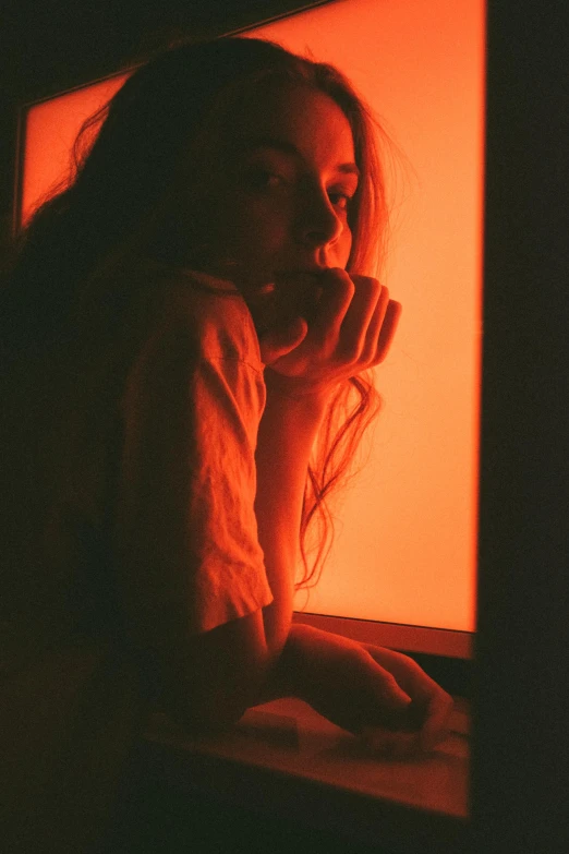 a woman sitting in front of a red light, inspired by Elsa Bleda, unsplash contest winner, red and orange glow, leaning against the window, expired color film, glowing in the dark