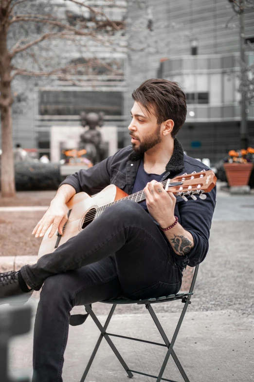 a man sitting in a chair playing a guitar, inspired by Germán Londoño, pexels contest winner, in a city square, background : diego fazio, lindsay adler, looking to the side off camera