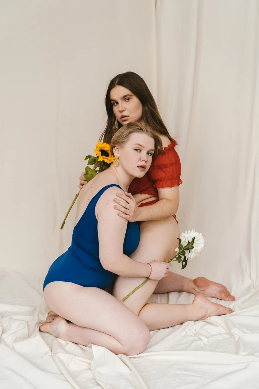 a couple of women sitting on top of a bed, an album cover, unsplash, renaissance, porcelain pale skin, dark blue leotard costume, tall flowers, blue or red