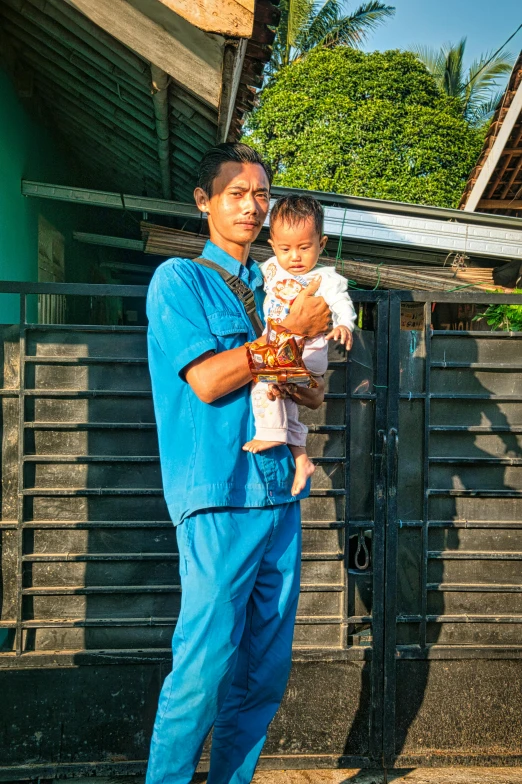 a man holding a baby in his arms, sumatraism, healthcare worker, standing outside a house, hero, father figure image