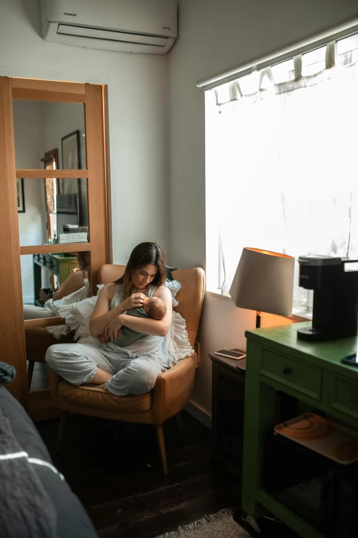 a woman sitting in a chair in a bedroom, a picture, by Everett Warner, unsplash, hugging and cradling, milk, hotel room, dwell