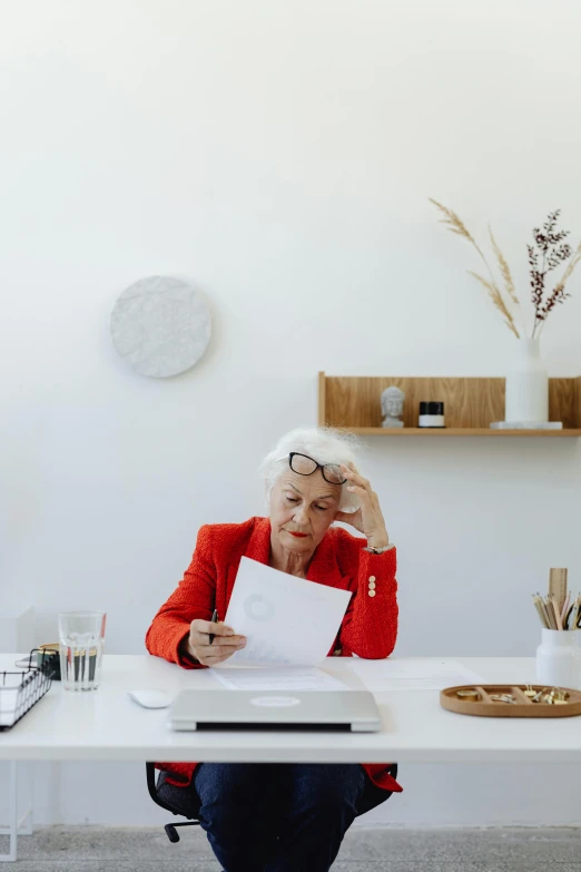 a woman sitting at a desk holding a piece of paper, pexels contest winner, minimalism, white-haired, busy, instagram post, home office