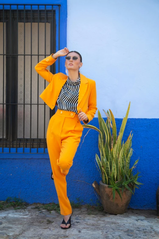 a woman in an orange suit leaning against a blue wall, inspired by Gina Pellón, trending on pexels, maximalism, colors: yellow, wearing a pinstripe suit, monochrome, sun set