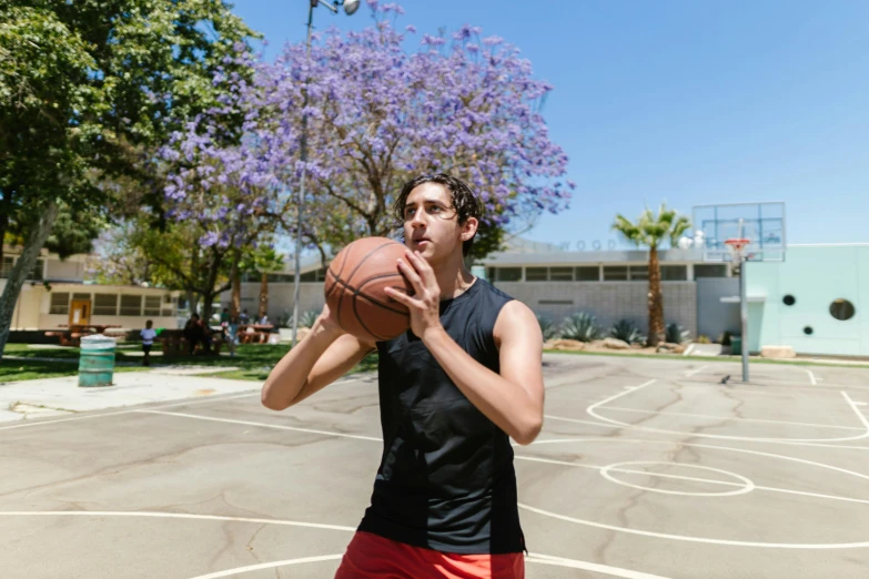 a man standing on a basketball court holding a basketball, by Gavin Hamilton, pexels contest winner, wearing a tank top and shorts, hila klein, mid - action, full faced