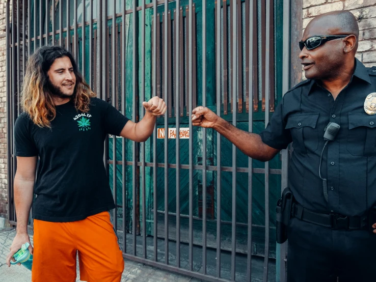 a couple of men standing next to each other, a colorized photo, pexels contest winner, symbolism, wearing orange prison jumpsuit, a black man with long curly hair, police state, reaching out to each other