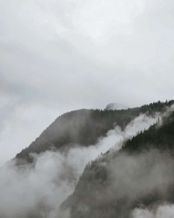 a large body of water with a mountain in the background, fog filled, on top of a mountain, the sky is gray, the photo was taken from afar